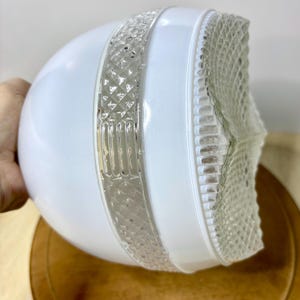 May include: A white glass light fixture globe featuring a clear, textured band with a diamond pattern and vertical ribbed accents. The globe has a smooth, rounded body and a distinct, faceted clear glass base with a grid-like embossed design.