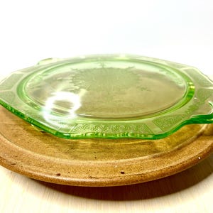 May include: A vintage green glass plate with a floral design sits atop a round, brown, wooden plate. The green plate has an octagonal shape with decorative edges. The wooden plate has a natural, rustic appearance.