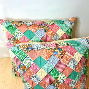 May include: Two rectangular throw pillows with a patchwork design. The pillows feature a variety of fabrics in pink, green, blue, and yellow, with floral, polka dot, and gingham patterns. The edges are trimmed with a ruffled fabric.