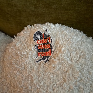 May include: A black and red sticker with the text "I can't even read" and a stylized illustration of a wolf. The sticker is placed on a white, textured surface.