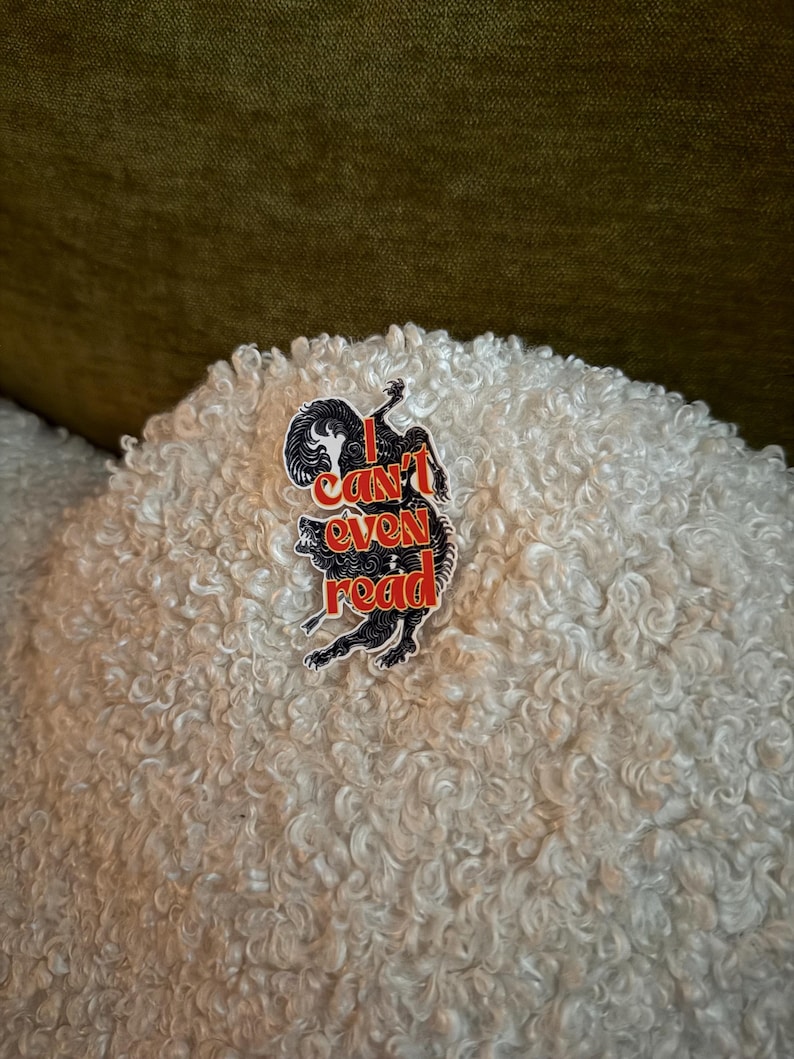 May include: A black and red sticker with the text "I can't even read" and a stylized illustration of a wolf. The sticker is placed on a white, textured surface.