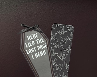 May include: Two black and white bookmarks. One bookmark is shaped like a coffin with the text "Here lies the last page I read". The other bookmark has a pattern of white origami cranes on a black background.