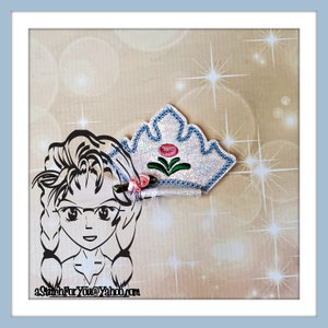 May include: A white and blue crown with a pink flower and green leaves. The crown is decorated with glitter and has a satin ribbon attached.