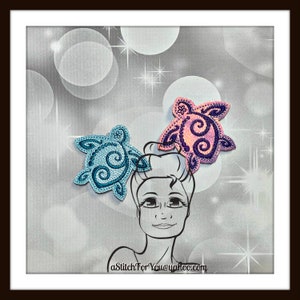 以下が含まれることがあります： 渦巻き模様の青い刺繍とピンクの刺繍の2つのウミガメのデザイン。デザインは銀色のグリッター効果のある白い背景です。