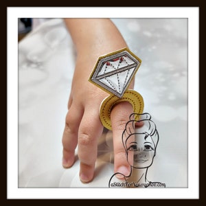 May include: A gold ring with a large silver diamond on top. The ring is on a finger and the diamond is pointing up.
