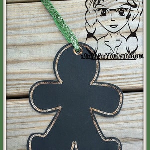 May include: Black gingerbread man ornament with gold glitter trim. The ornament is hanging from a green glitter ribbon.
