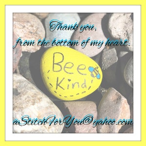 May include: A yellow painted rock with the words "Bee Kind" written on it. The rock is surrounded by other rocks and the text "Thank you, from the bottom of my heart. aStitchForYou@yahoo.com" is written on the image.