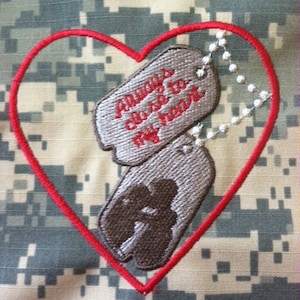 Op de afbeelding: Een geborduurde patch in de vorm van een rood hart, met daarin twee zilveren hondenpenningen. De bovenste hondenpenning heeft de tekst "Altijd dicht bij mijn hart".