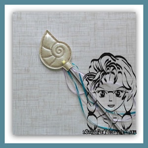 May include: A silver seashell-shaped wand with a silver stick and a light blue and purple ribbon. The wand is on a light brown textured background.