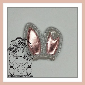 May include: A pair of sparkly silver bunny ears with pink metallic accents. The ears are sewn with a glittery fabric and have a raised, textured design.