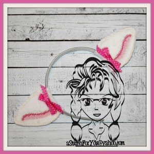May include: A white headband with two white felt bunny ears with pink polka dot bows. The headband is decorated with a black and white illustration of a girl with pigtails wearing glasses.