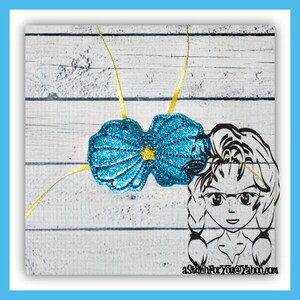 Può includere: Una coppia di maschere per gli occhi a forma di conchiglia di mare blu glitterata con lacci in nastro dorato. Le maschere per gli occhi sono su uno sfondo di legno bianco. Il testo "aStitchForYou@Yahoo.com" è nell'angolo in basso a destra dell'immagine.