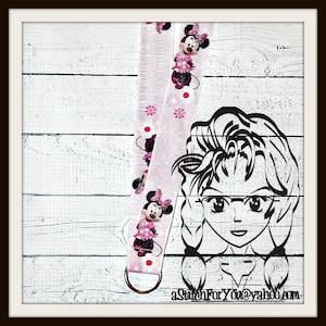 May include: Pink and white ribbon with a Minnie Mouse print. The ribbon has a gold metal ring attached to one end. The ribbon is on a white wooden background. The text "aStitchForYou@yahoo.com" is in the lower right corner of the image.