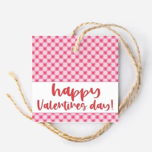 May include: A pink and white gift tag with a checkered pattern of pink hearts. The tag has a white label with the text "happy valentines day!" in red.