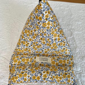 May include: A triangular pillow with a floral pattern of yellow flowers and navy blue leaves on a white background. The pillow has a label that reads "COOPER'S CORNER".