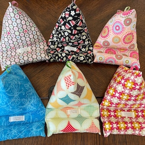 May include: Six fabric book stands in various patterns. Designs include floral, geometric, and dragonfly prints in colours like pink, black, blue, and yellow. Each stand has a small label that reads "COOPER'S CORNER".