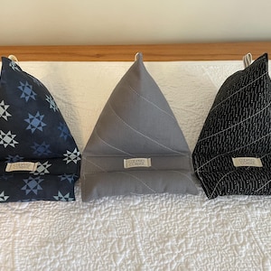 Puede incluir: Tres sujetalibros triangulares en azul marino con patrones de estrellas, gris con líneas cosidas y negro con líneas punteadas blancas. Cada uno tiene una pequeña etiqueta que dice "COOPER'S CORNER". Estos soportes de tela están diseñados para sostener libros.