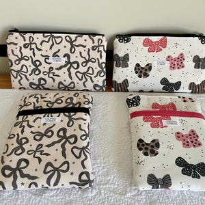 May include: Four fabric pouches with zipper closures. Two pouches feature a cream background with a pattern of black bows and stars. The other two pouches have a white background with a pattern of bows in black, pink, and brown.