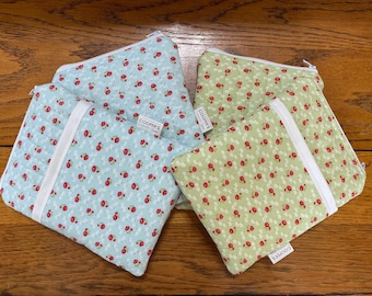 May include: Four quilted pouches with floral patterns. Two pouches are light blue with red flowers, and two are light green with red flowers. Each pouch has a white zipper and a white fabric strip. The pouches are labeled "COOPER'S".