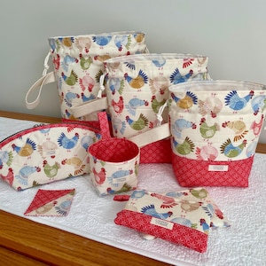 May include: A collection of fabric items featuring a chicken pattern. The set includes drawstring bags, a zippered pouch, a small cup, and coasters. The main fabric is cream-colored with colorful chickens, and the bottom and accents are red.