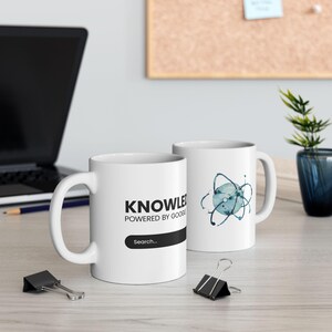 May include: Two white ceramic mugs. One mug has the text "KNOWLEDGE POWERED BY GOOGLE" with a search bar. The other mug has a blue and teal watercolor atom design. Both mugs have a white handle.