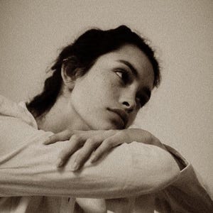 May include: Sepia-toned portrait of a person with dark hair and fair skin, resting their head on their arm. The person is looking off to the side, with a thoughtful expression. The image is softly lit, creating a vintage aesthetic.