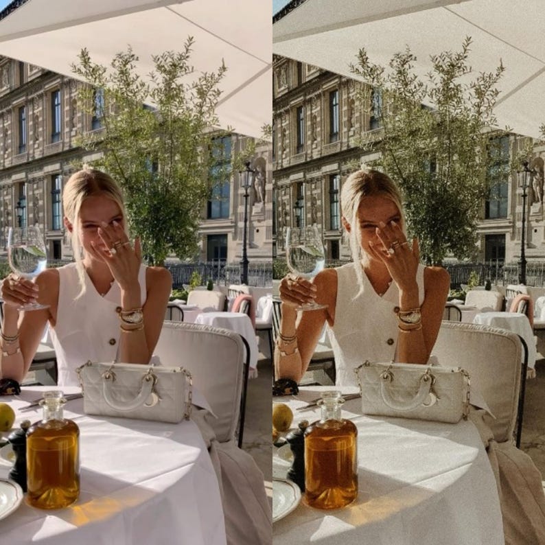 May include: A woman wearing a white sleeveless dress sits at a table outside a cafe. She is holding a glass of white wine and smiling. There is a white handbag on the table next to a bottle of olive oil.