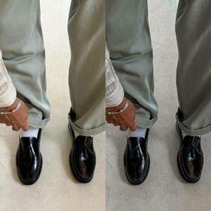 May include: A pair of black leather tassel loafers with a white sock peeking out from the top. The loafers are worn by a person wearing green pants.