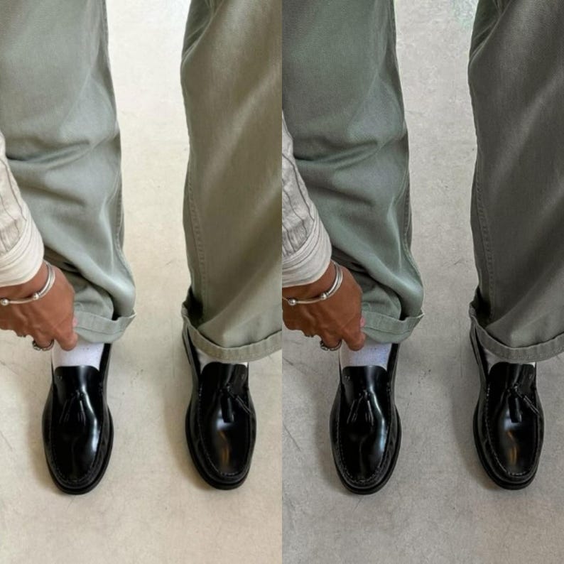 May include: A pair of black leather tassel loafers with a white sock peeking out from the top. The loafers are worn by a person wearing green pants.