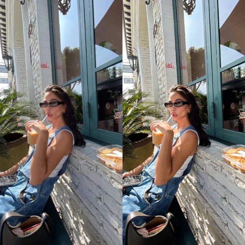 May include: A woman wearing a white tank top and blue denim overalls is sitting outside a cafe. She is holding a cup of iced coffee and wearing sunglasses.