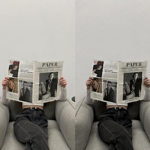 May include: A person sitting in a gray armchair, reading a magazine with the word "PAPER" on the cover. The magazine features black and white photos of models.