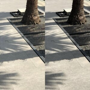 May include: A close-up of a palm tree trunk with a black metal grate surrounding it. The grate is set into a concrete walkway with a light gray surface. The tree trunk is brown and has a rough texture. The grate is made of thin metal bars that are spaced evenly apart. The walkway is clean and free of debris.