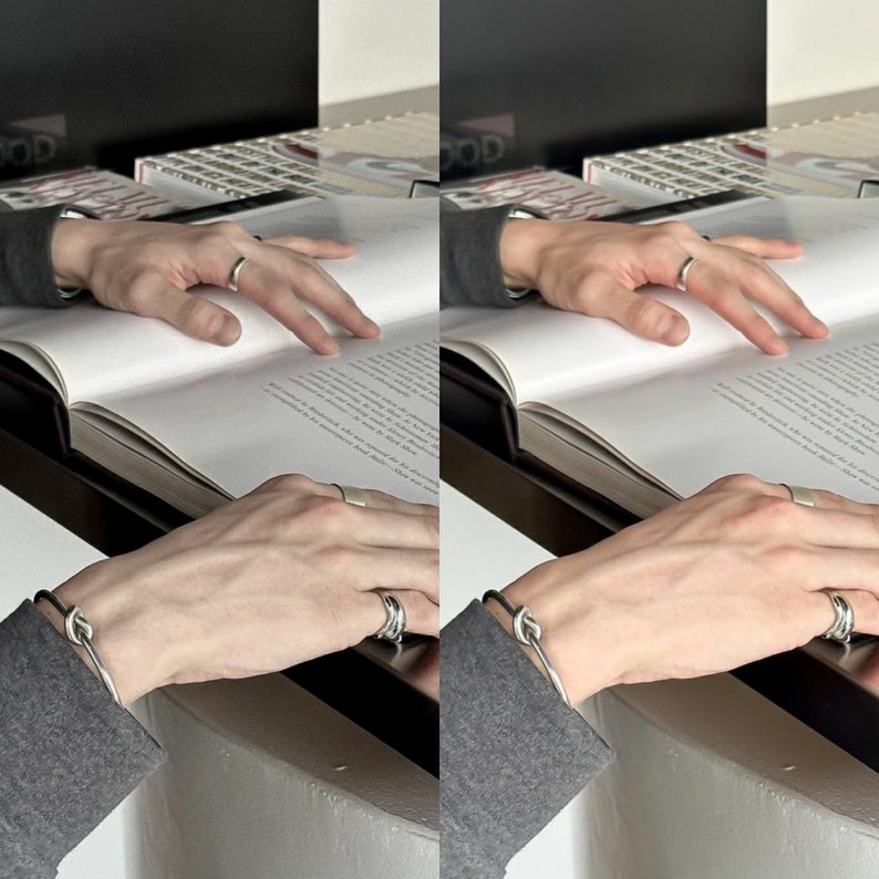 May include: Two hands wearing silver rings and bracelets. One hand is holding a book open, while the other hand is resting on the book. The book is open to a page with text.