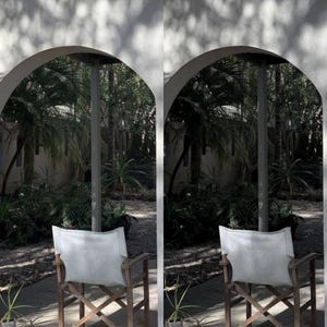 May include: Two white canvas director's chairs with wooden frames sit facing each other on a patio. The chairs are positioned under an archway with a view of lush green foliage.