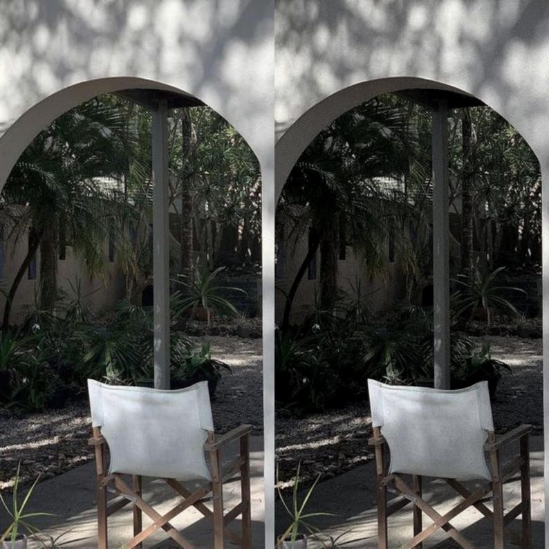 May include: Two white canvas director's chairs with wooden frames sit facing each other on a patio. The chairs are positioned under an archway with a view of lush green foliage.