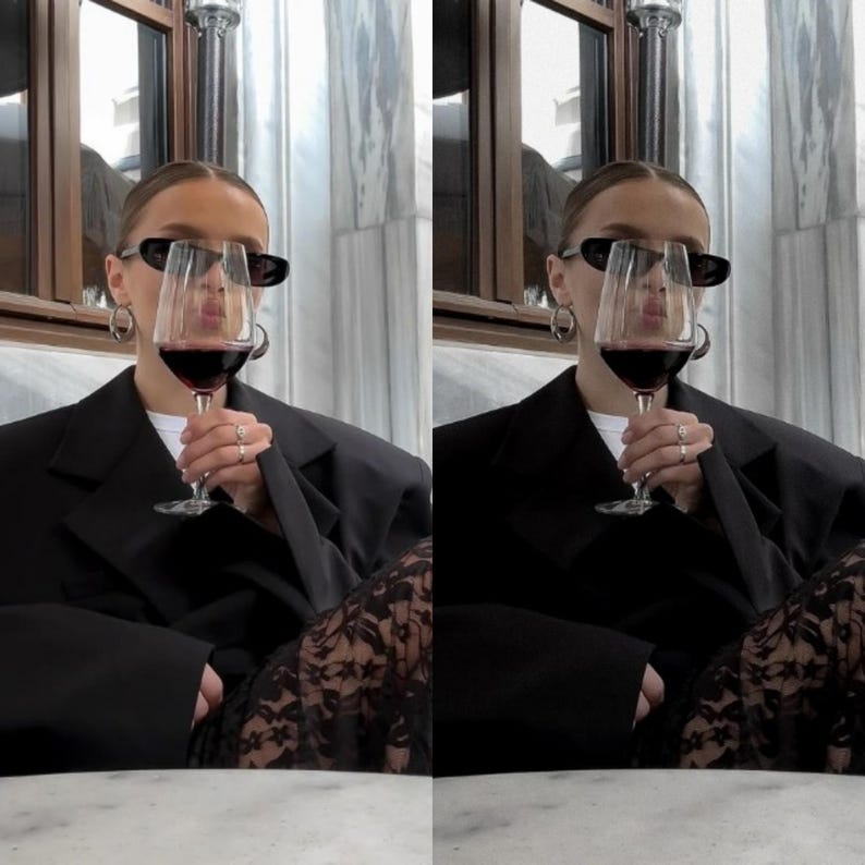 May include: A person wearing a black blazer and lace skirt holds a glass of red wine. They are wearing thin, black framed sunglasses.