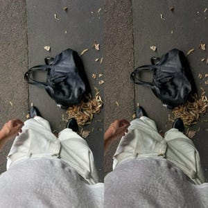 May include: A person wearing white pants and a grey shirt is standing on a sidewalk with a black leather tote bag and fallen leaves.