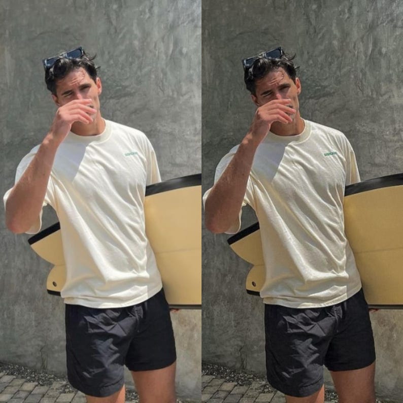 May include: A person wearing a white t-shirt with a green logo and black swim trunks is holding a surfboard. The person is wearing sunglasses and has their hand over their face.