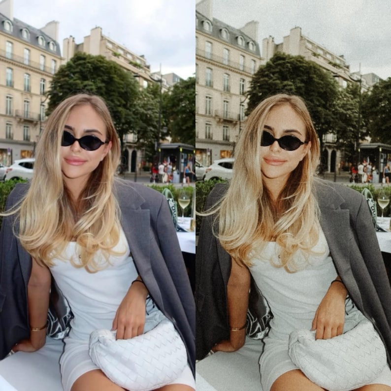 May include: A woman wearing a white dress and a gray blazer sits at an outdoor cafe table. She is wearing black oval sunglasses and a white woven handbag. The cafe is located in a city with buildings in the background.