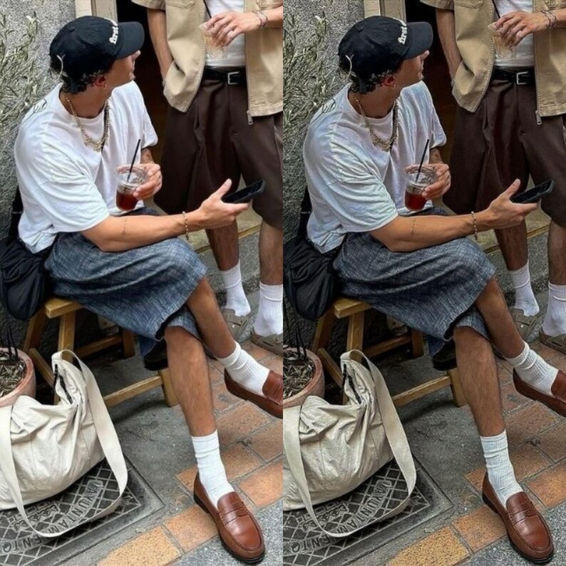 May include: Two people wearing white t-shirts, black baseball caps, and blue and white striped shorts are sitting on wooden stools. They are both holding a cup of iced coffee and a phone. They are wearing white socks and brown leather loafers.