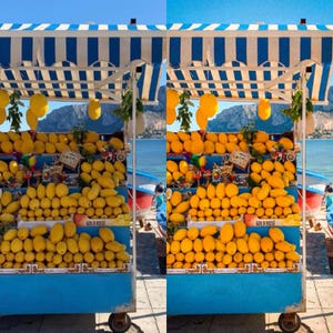 May include: A blue and white striped wooden stand with a blue base, filled with yellow lemons and mangoes. The stand is on a beach with a blue sky and water in the background. The stand has a sign that says "Gold Rose".