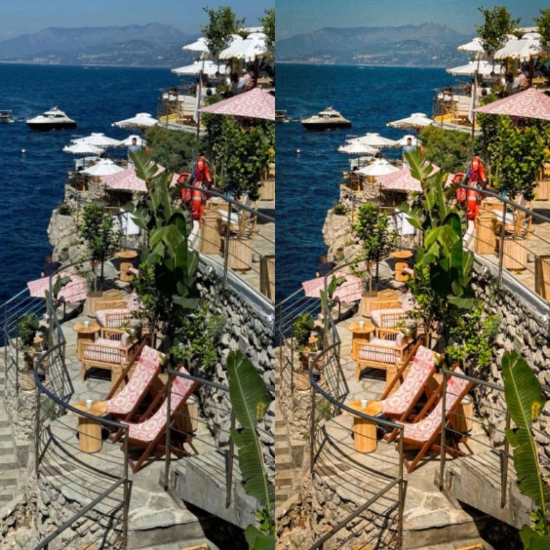 May include: A view of a cliffside restaurant with tables and chairs set up on a stone patio. The restaurant is overlooking a blue ocean with boats in the distance. There are red and white umbrellas and lush green plants.