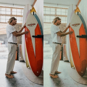 K&ouml;nnte beinhalten: Eine Person steht neben einer Wand mit drei Surfboards, die daran h&auml;ngen. Die Surfboards sind alle in verschiedenen Farben und haben unterschiedliche Designs. Die Person tr&auml;gt ein wei&szlig;es Hemd und eine beige Hose. Die Surfboards sind alle lang und schmal, mit einer abgerundeten Nase und einem spitzen Heck.