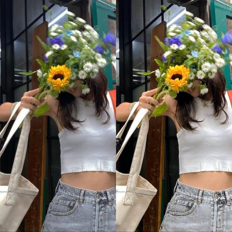 May include: A person wearing a white tank top and blue jeans is holding a bouquet of flowers in front of their face. The flowers include sunflowers, daisies, and blue flowers.