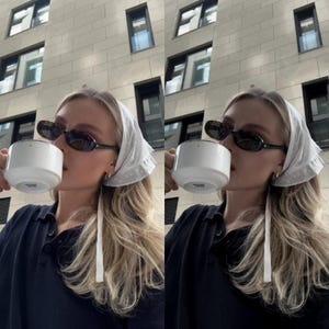 May include: A woman wearing a white headscarf with a black polo shirt and sunglasses is drinking from a white mug.