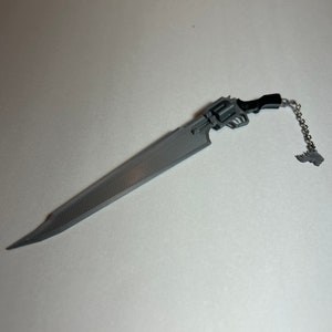 Puede incluir: Una espada gris impresa en 3D con un mango negro y una cadena unida a un pequeño amuleto gris.