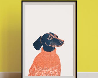 May include: A framed art print featuring a dachshund wearing an orange sweater. The dog is depicted with a black head and ears, and the sweater has a textured pattern. The background is white, and the frame is black.