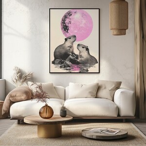 May include: A framed print of two capybaras looking up at a large pink moon. The capybaras are in a body of water with rocks and reflections.