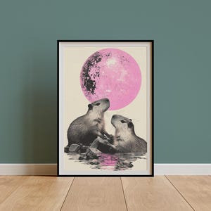 May include: A framed print of two capybaras looking at each other in front of a large pink disco ball.