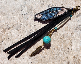 May include: A blue and white leather feather keychain with black tassels, a turquoise bead, and a small gold feather charm.